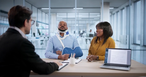 Worker wearing neck brace speaking with suited man across desk